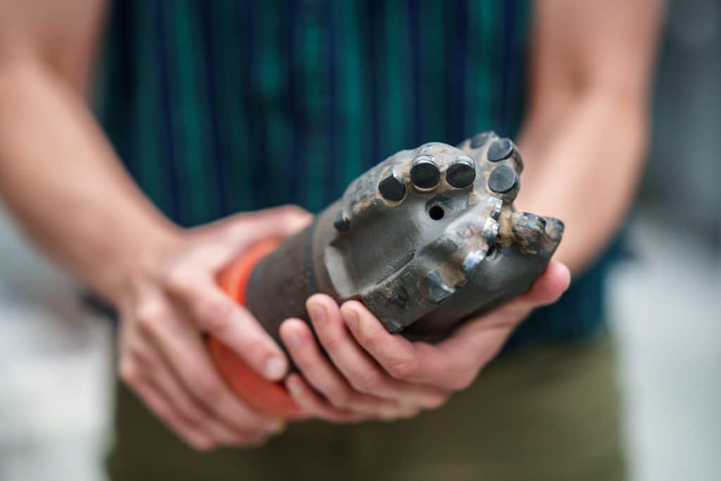 Sandia-drill-bit-1024×683 Mechanical engineer Melanie Schneider of Sandia National Laboratories holds a polycrystalline diamond compact (PDC) drill bit. After decades of research, PDC bits have only recently become practical for geothermal well drilling. (Photo: Craig Fritz / Sandia National Laboratories)