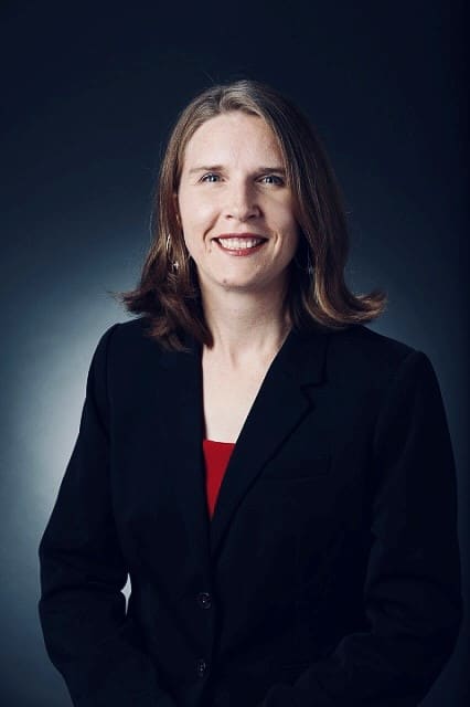 Professional headshot of Dr. Kristie S. McLin wearing a black blazer and red top, smiling against a dark blue gradient background.